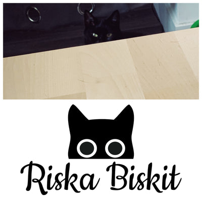 Riska peeps over the edge of the table, only her eyes and pointy black ears visible. The logo this photo inspired is below.